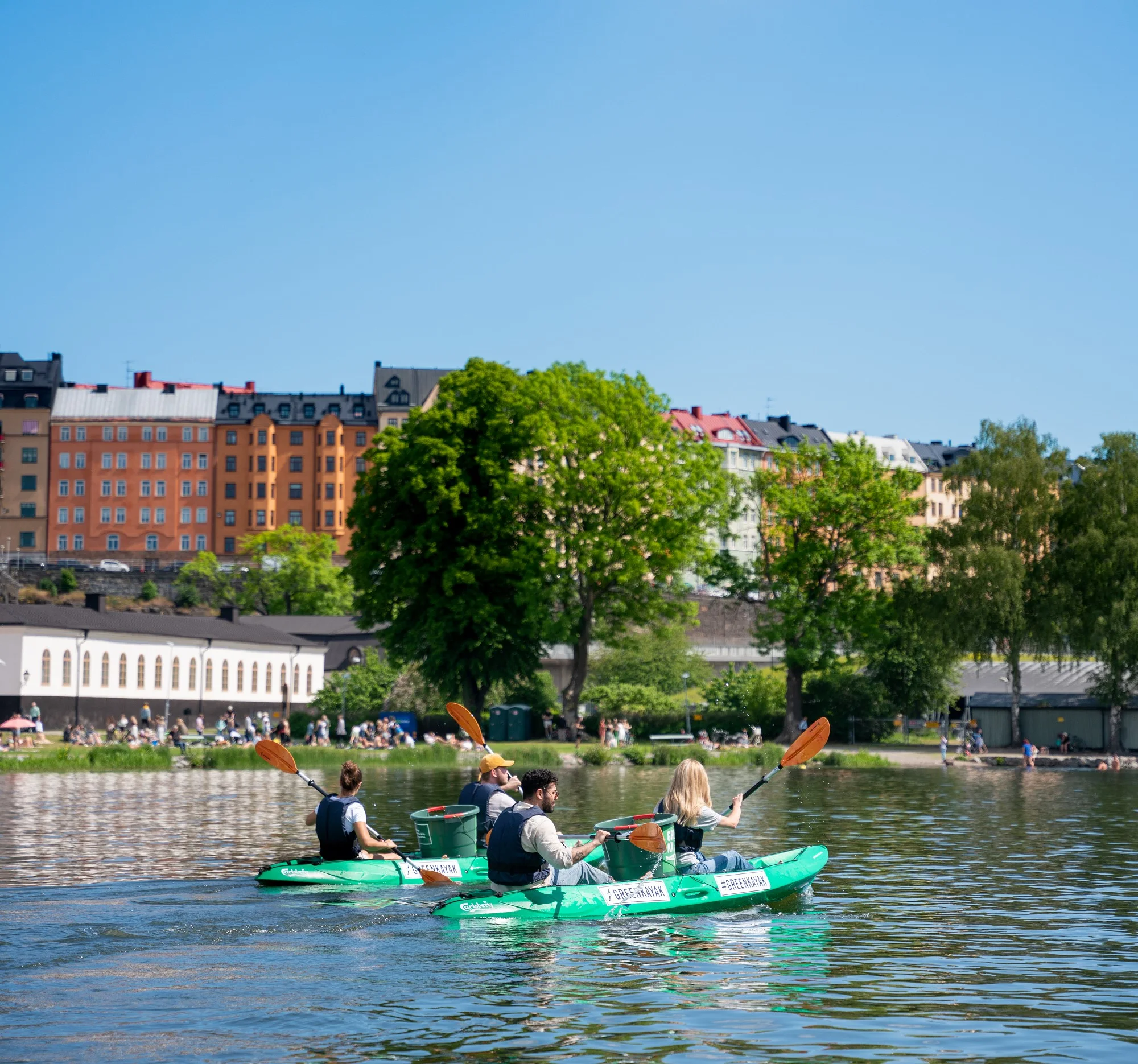 Two green GreenKayak kayaks paddling in front of the buildings of Södermalm